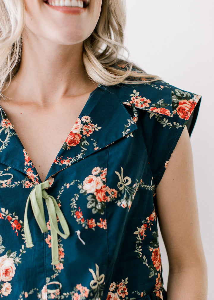 Close up o exaggerated collar and v-neck with a green tie on a navy capped sleeve top with floral.