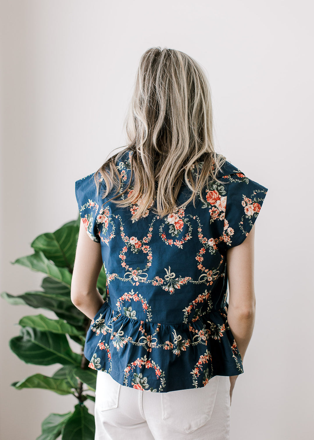 Back view of Model wearing a navy top with pink floral, exaggerated collar and cap sleeves. 