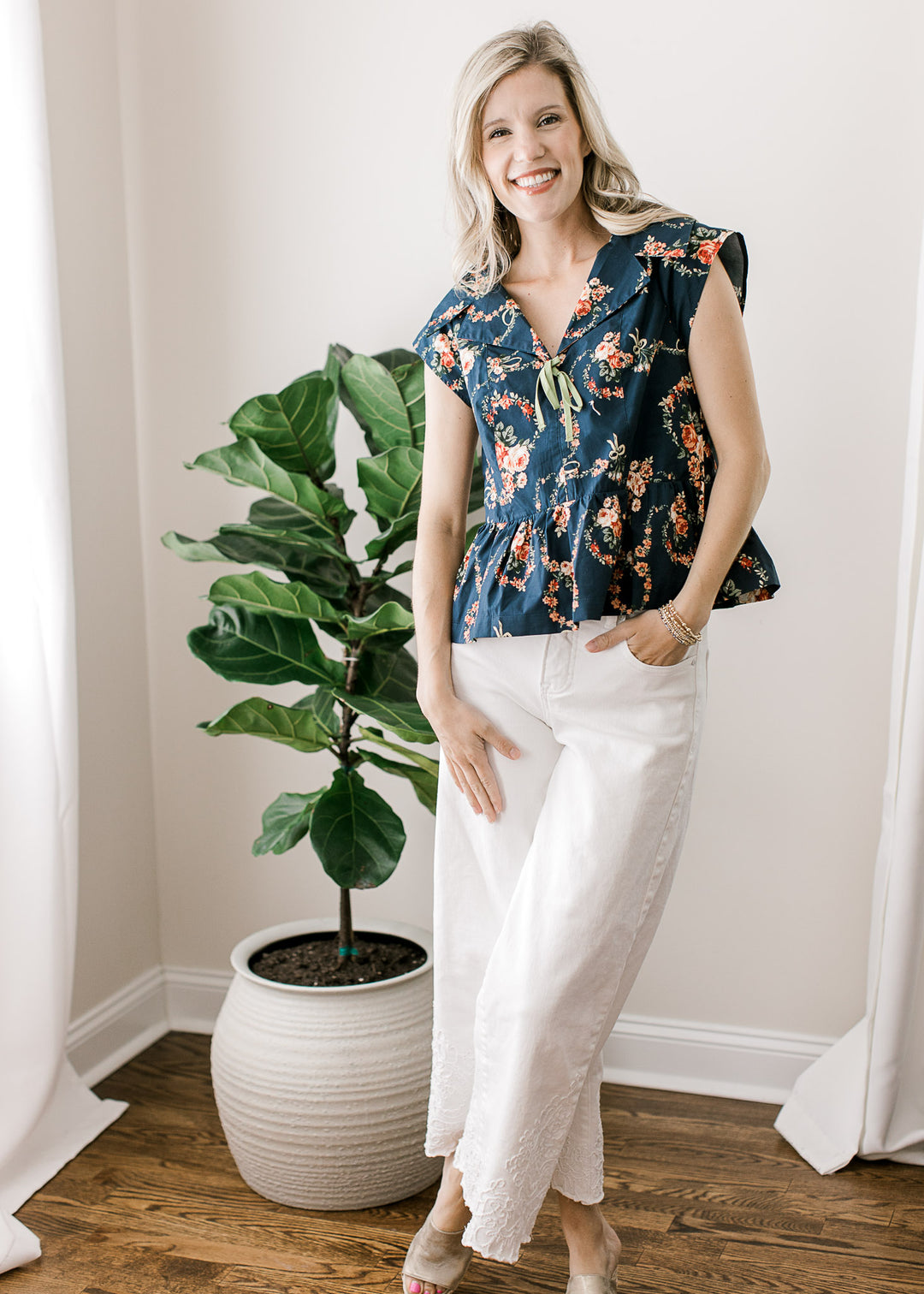 Model wearing white pants and a navy top with pink floral, v-neck with green bow and a collar.