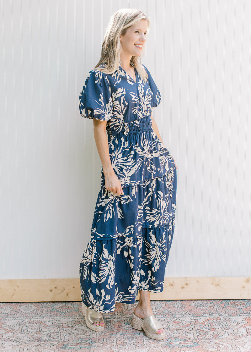 Model wearing a navy v-neck  maxi with cream floral, smocked waist and puff short sleeves.