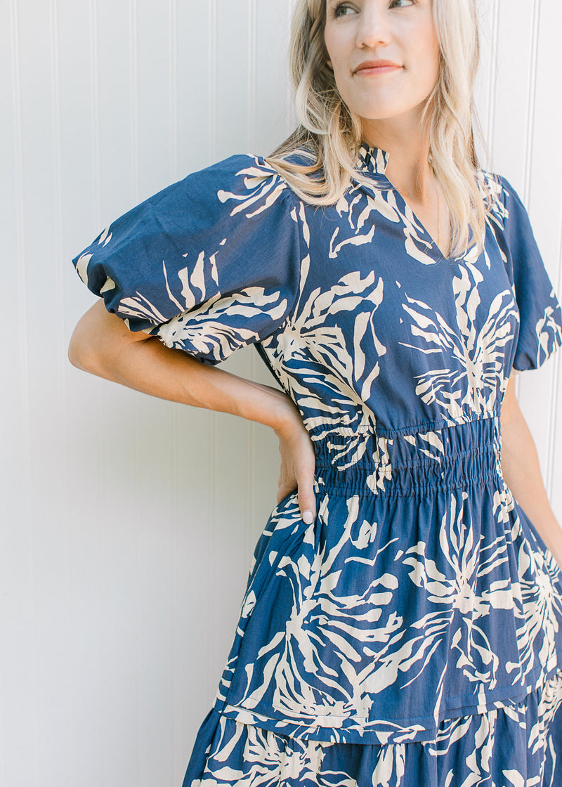 Close up of short puff sleeve, smocked waist and v-neck on a navy maxi with cream flowers.