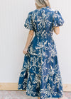 Back view of Model wearing a navy maxi with cream floral, smocked waist and puff short sleeves.