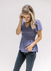 Model wearing a blue/violet v-neck top with gathered peplum, smocked bodice and short  sleeves.