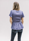 Back view of Model wearing a blue/violet top with gathered peplum, smocked bodice and short sleeves.
