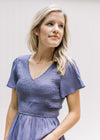 Close up of smocked bodice and flutter short sleeves on a blue/violet v-neck top. 