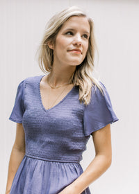 Close up of smocked bodice and flutter short sleeves on a blue/violet v-neck top. 