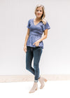 Model wearing jeans and booties with a blue/violet top with a smocked bodice and short sleeves.
