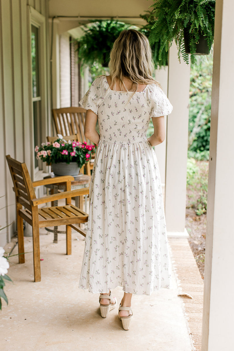 Back view of Model wearing a cream maxi with lavender floral, a smocked bodice and square back.