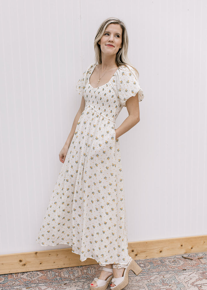 Model wearing a cream maxi with yellow floral, smocked bodice, pockets and bubble short sleeves. 