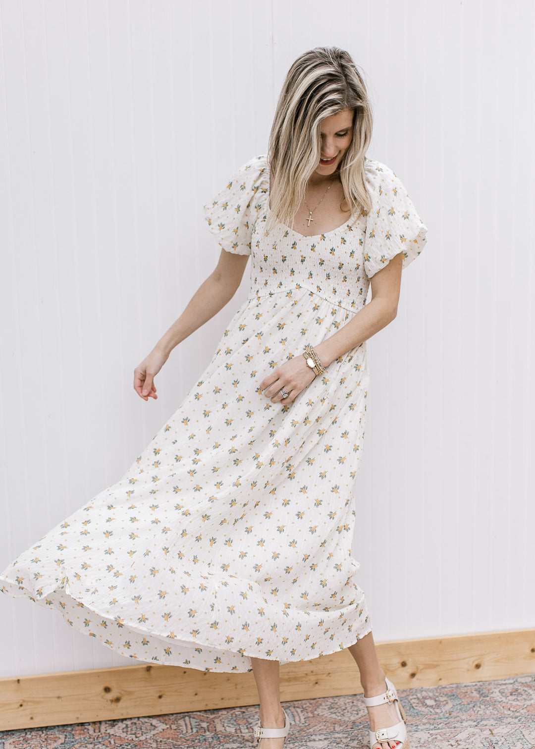 Model wearing heels and a cream maxi with yellow floral, smocked bodice and short sleeves. 