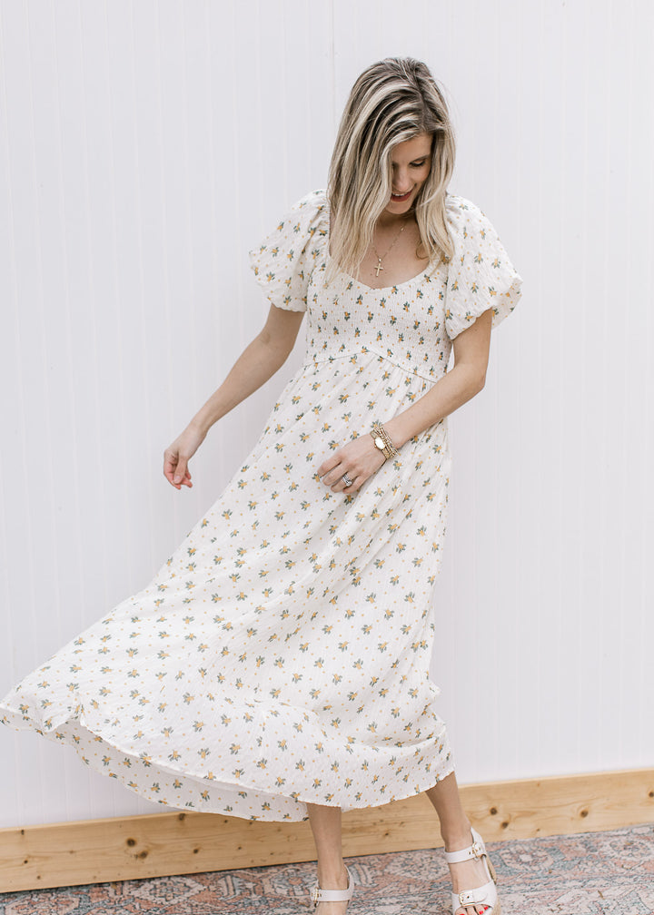 Model wearing heels and a cream maxi with yellow floral, smocked bodice and short sleeves. 