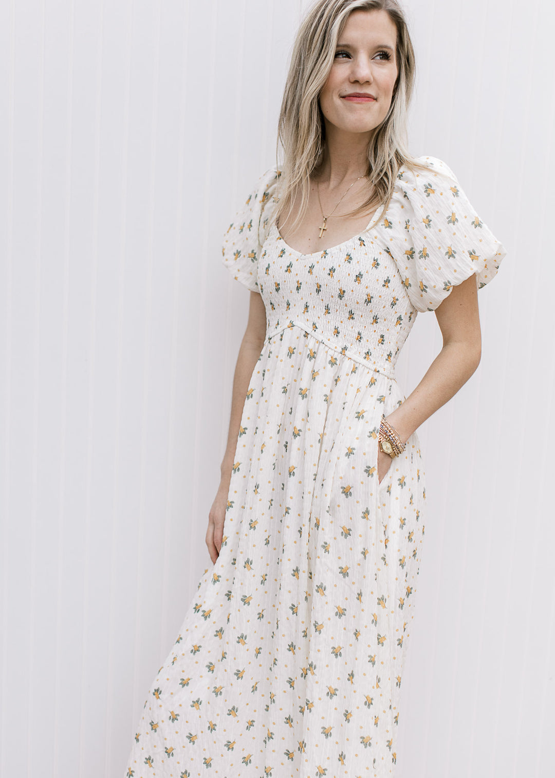 Model wearing a cream maxi with yellow floral, smocked bodice, pockets and a flowy skirt. 