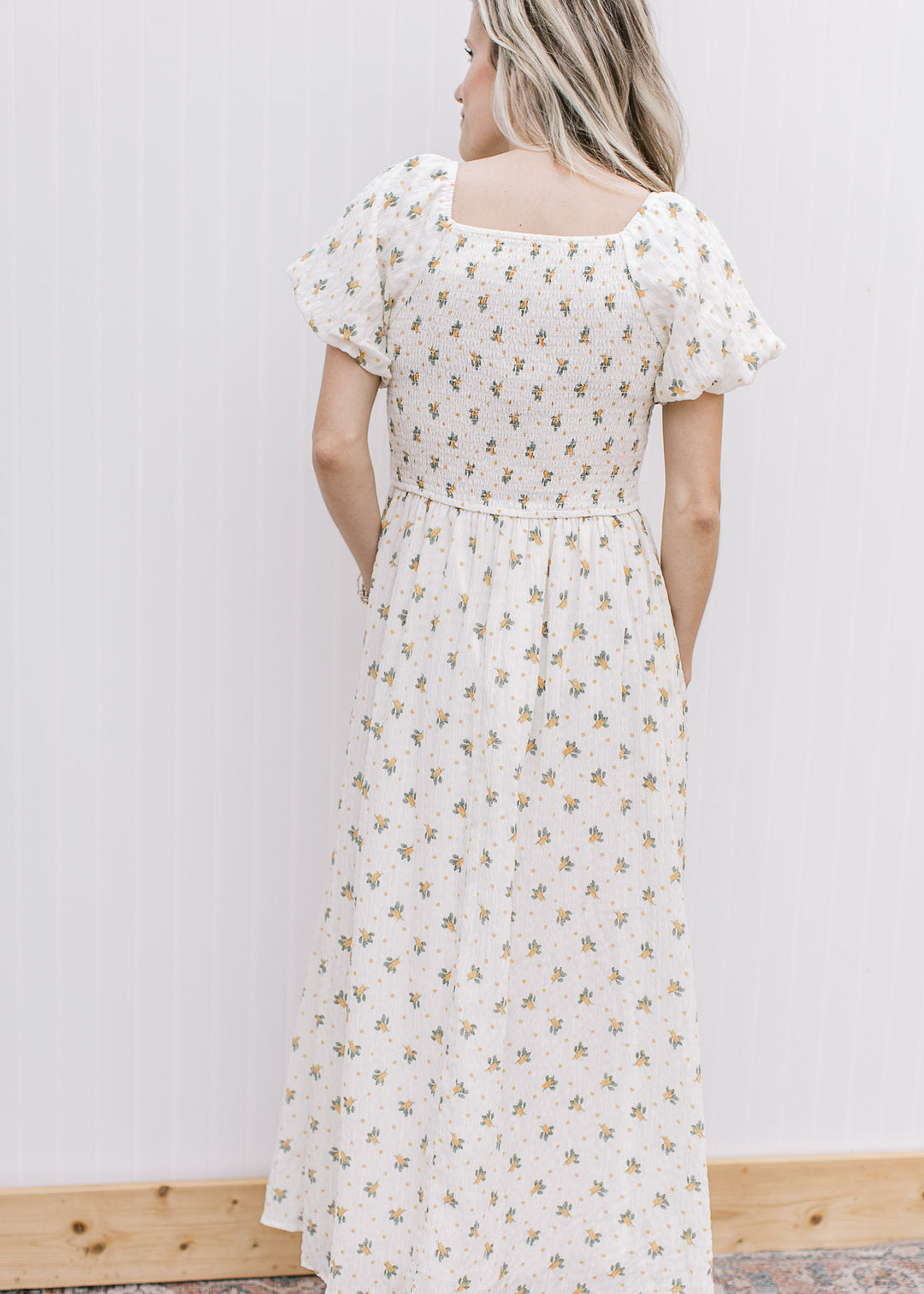 Back view of Model wearing a cream maxi with yellow floral, smocked bodice and square neckline. 