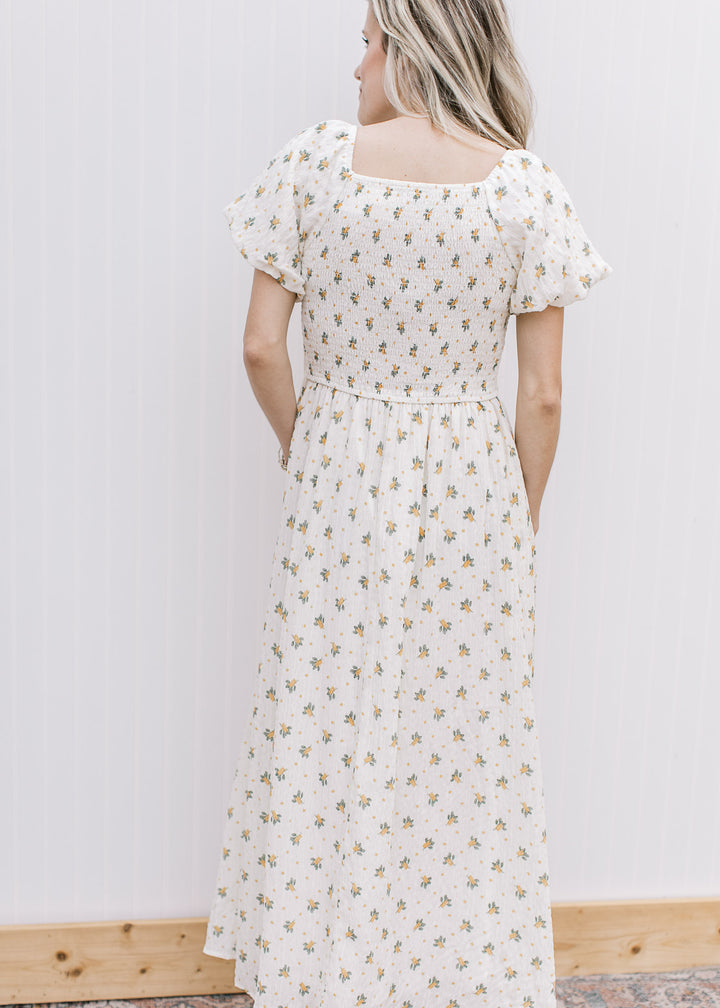 Back view of Model wearing a cream maxi with yellow floral, smocked bodice and square neckline. 