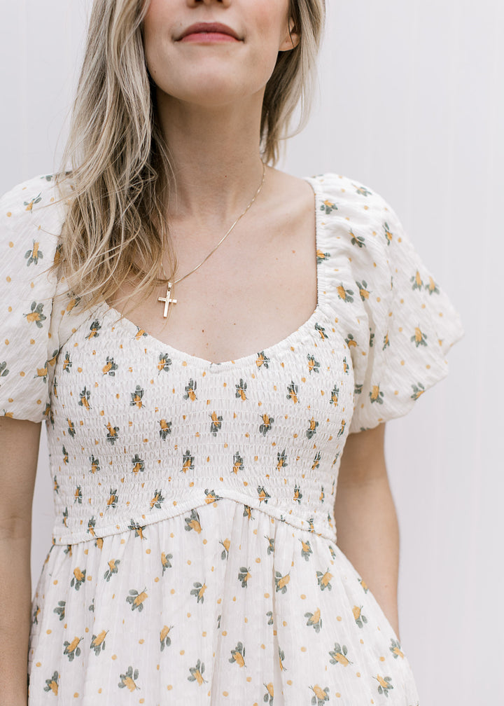 Close up of smocked bodice, v-neck and bubble short sleeves on a cream maxi with yellow floral.