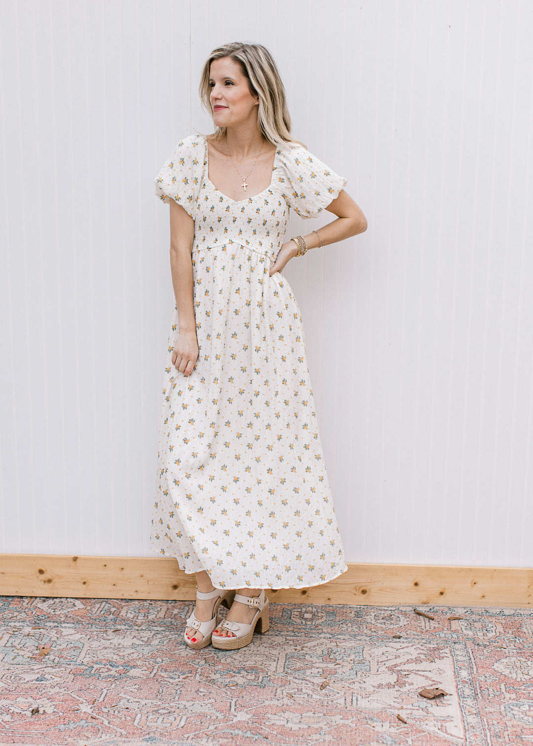 Model wearing a necklace, heels and a cream maxi with yellow floral and smocked bodice. 