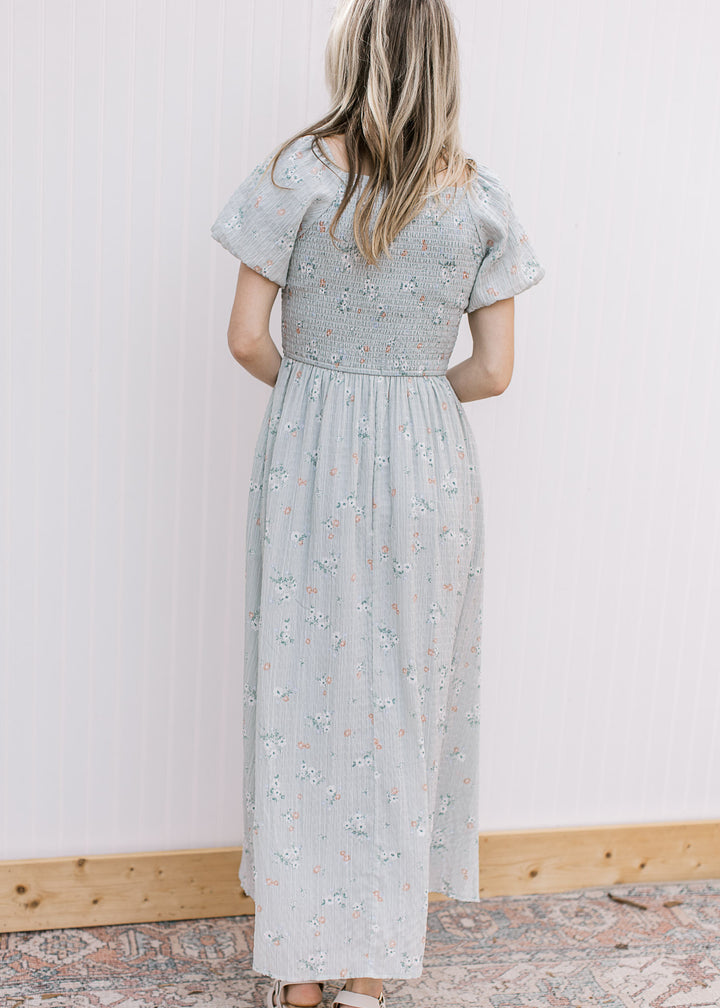 Back view of a model wearing a pale blue maxi with peach floral, smocked bodice and short sleeves.
