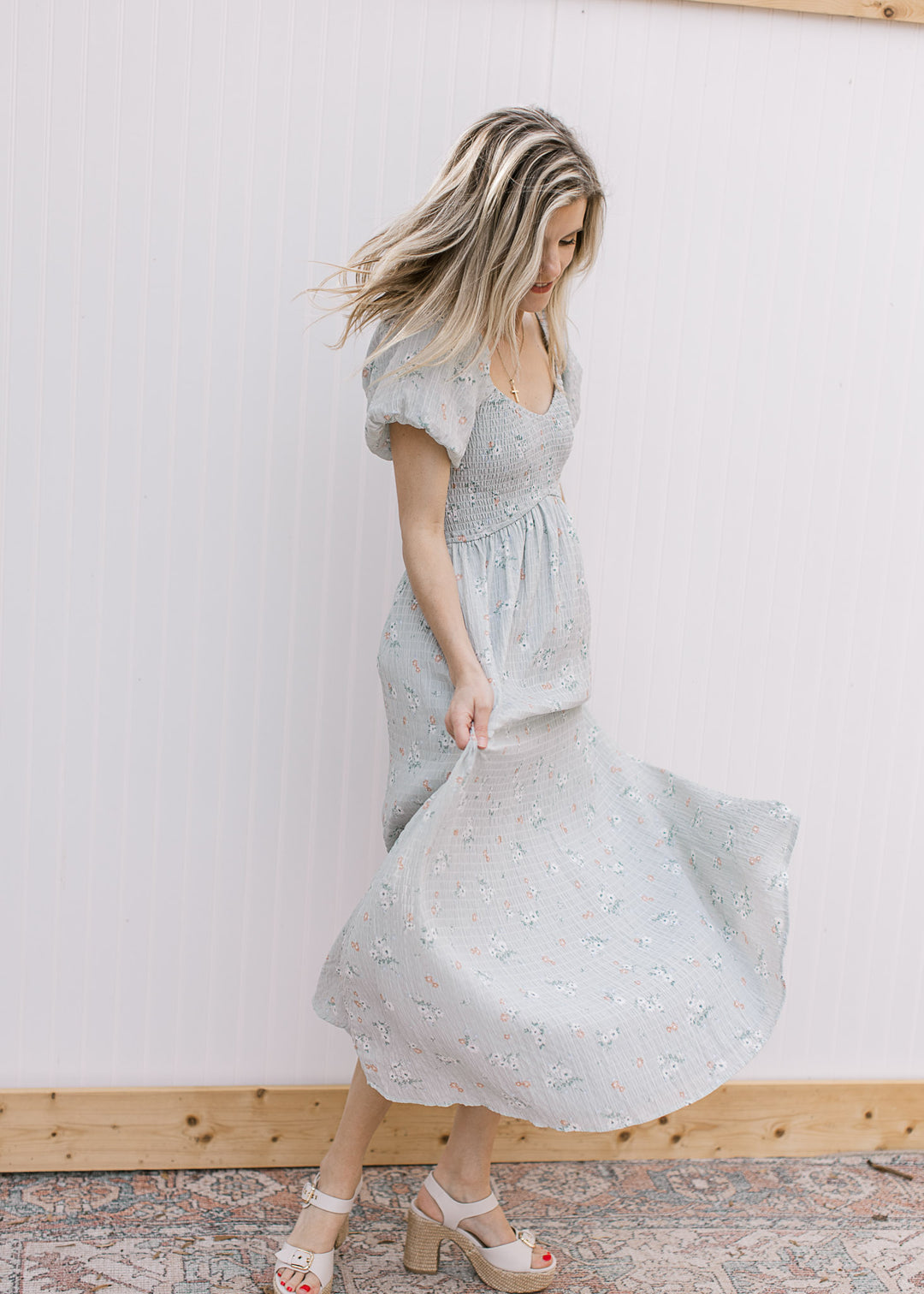 Model twirling in a pale blue maxi with peach and cream floral, smocked bodice and a v-neckline.