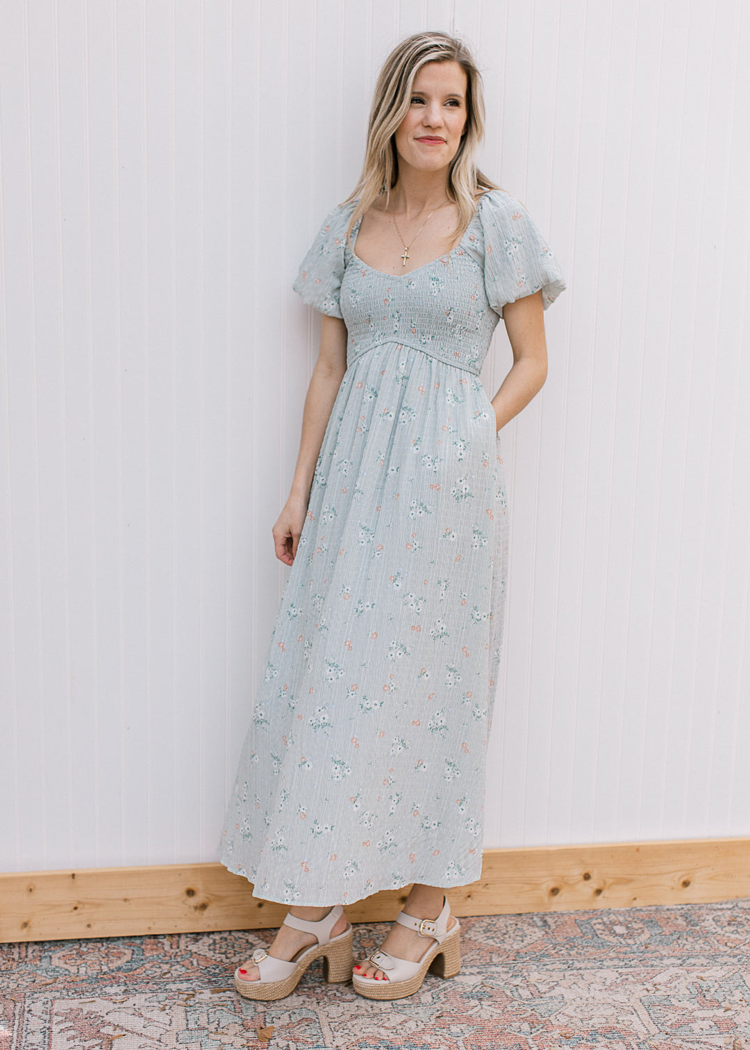 Model wearing heels and a pale blue maxi with floral, pockets, v-neck and bubble short sleeves. 