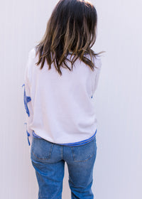 Back view of Model wearing a cream top with blue patch stars along the long sleeve and exposed hem. 