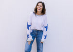 Model wearing jeans and a cream top with blue patch stars along the long sleeve and exposed hem. 