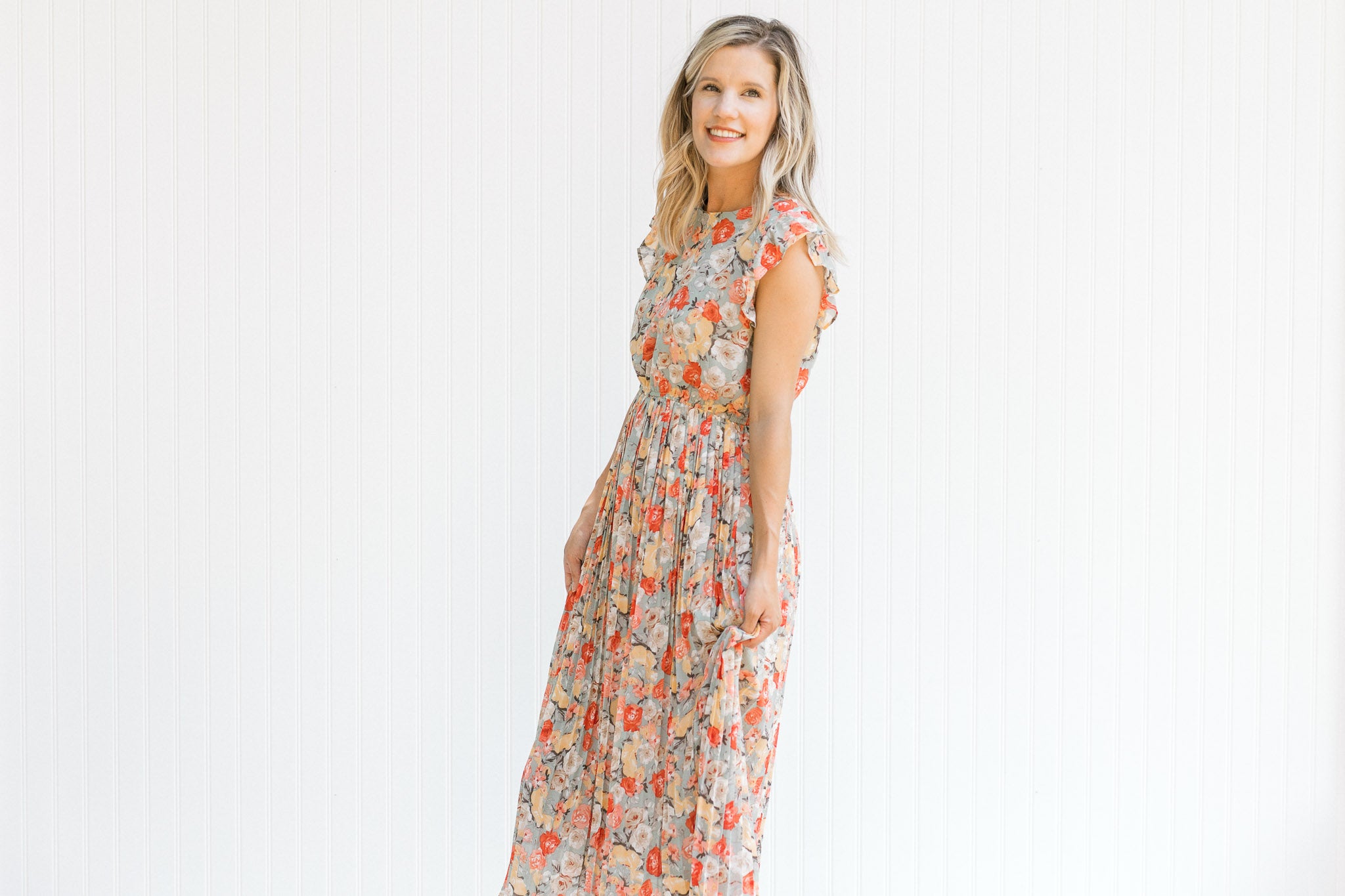 Model wearing a mint midi dress with a floral pattern, ruffle capped sleeve and a pleated skirt. 