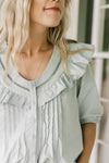 Close up of lattice detail and ruffle at the neck of a mint green top with 3/4 sleeves.