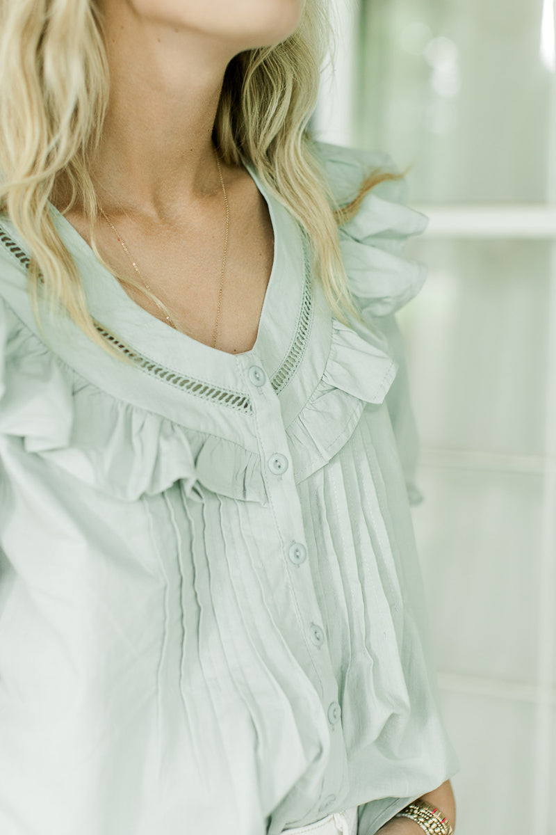 Close up of v-neck with ruffle and button front on a mint green top with pleating. 