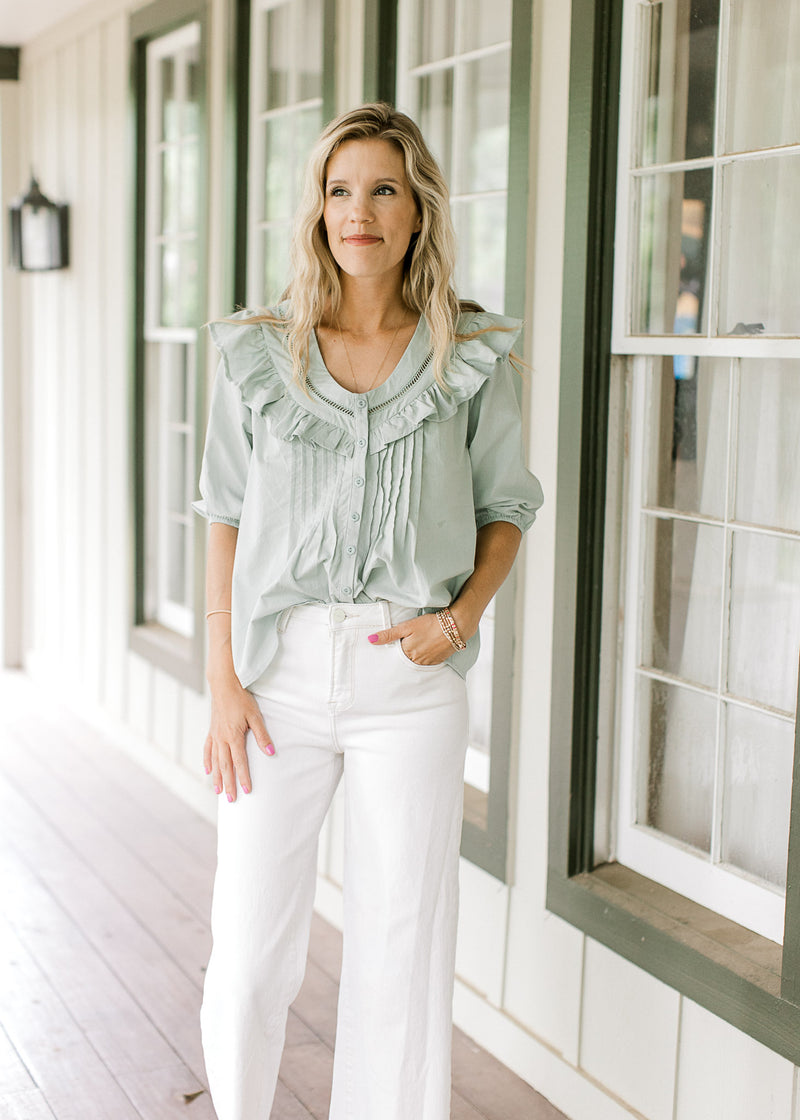 Model wearing a mint green top with pleating and lattice detail and a button front. 