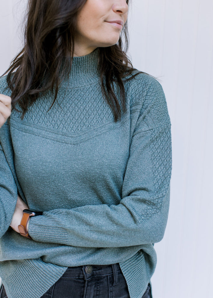 Close up of knit yolk detail on a model in a sage green top with a mock neck and long sleeves. 