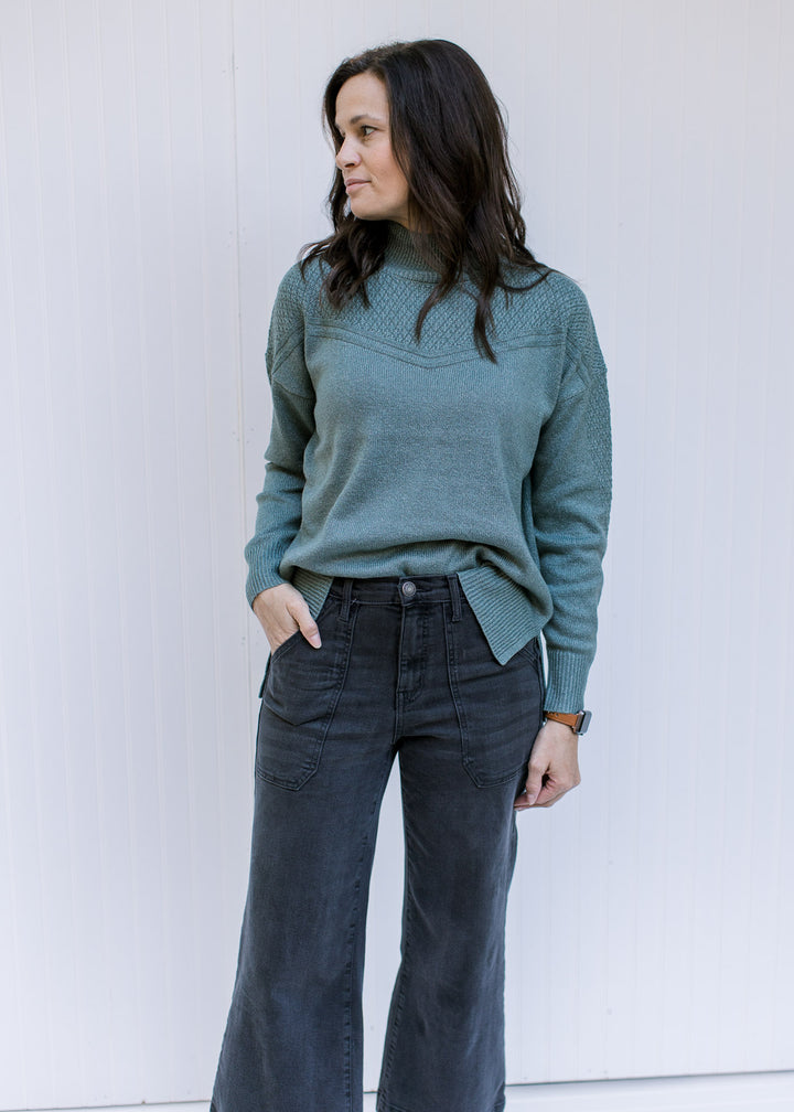 Model wearing jeans with a sage long sleeve top with a knit yolk detail and a mock neckline. 