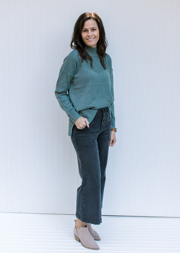 Model wearing jeans and booties with a sage long sleeve top with a knit yolk detail and a mock neck.