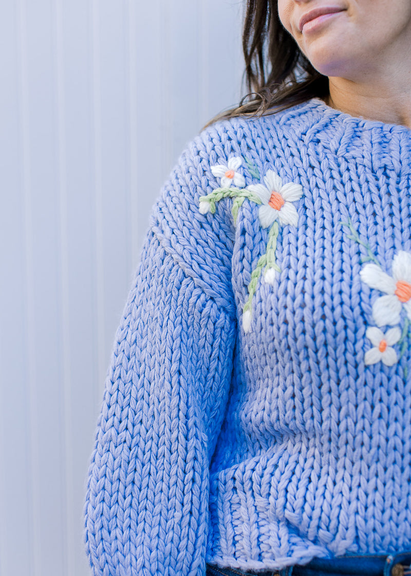 Close up of white flowers on a soft blue knit sweater with 3/4 sleeves and a round neck. 