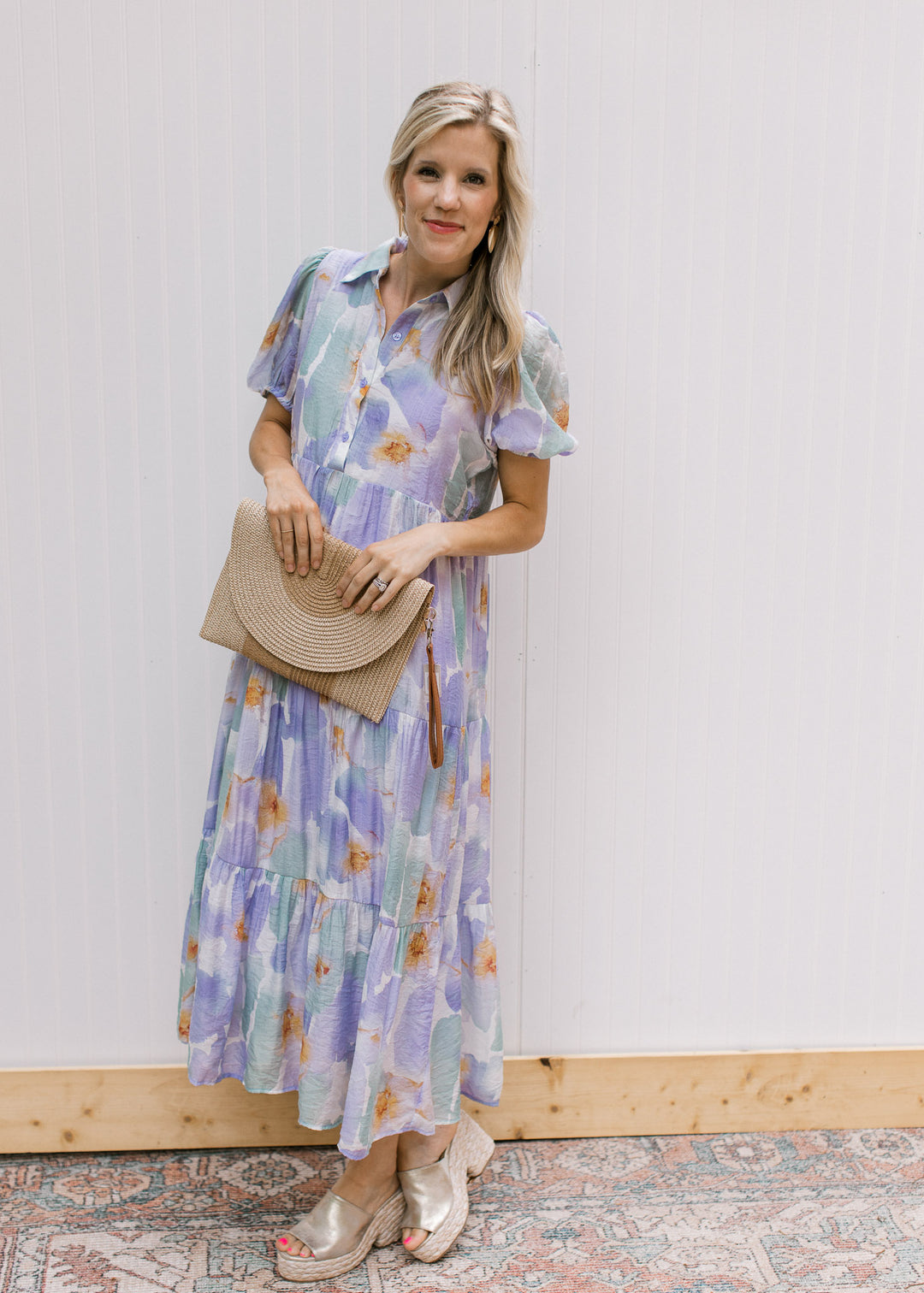 Model holding a purse wearing a cream dress with lavender and aqua watercolor. 
