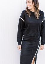 Model wearing a black matching sweater set with white details and a split on the skirt. 