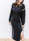 Model wearing a black matching sweater set with white details and a split on the midi skirt. 