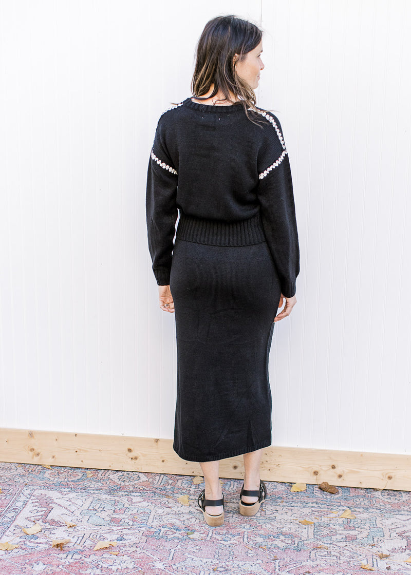 Back view of a black matching sweater set with white details and a split on the skirt. 