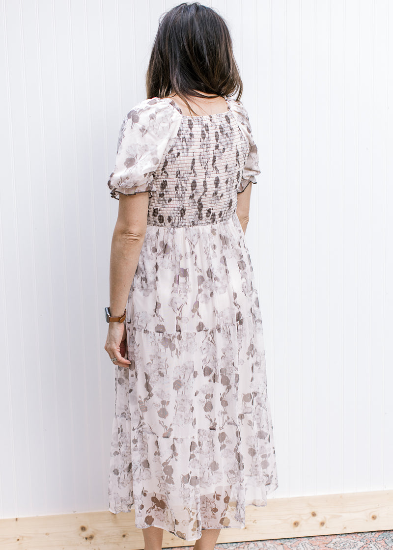 Back view of Model wearing a cream midi with gray floral, smocked bodice and bubble short sleeves.