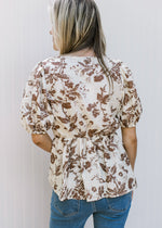 Back view of Model wearing a white top with mocha floral a peplum fit square neck and short sleeves.