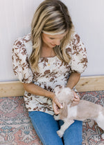 Model wearing jeans with a white top with mocha floral a peplum fit square neck and short sleeves. 