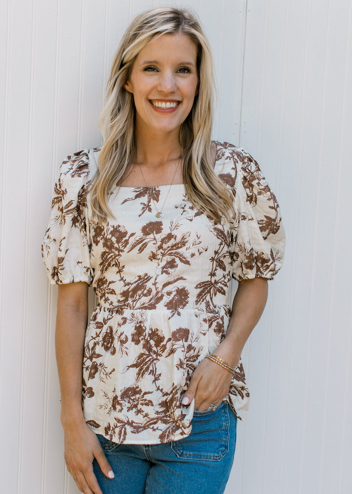 Model wearing a white top with mocha floral a peplum fit square neck and short sleeves.
