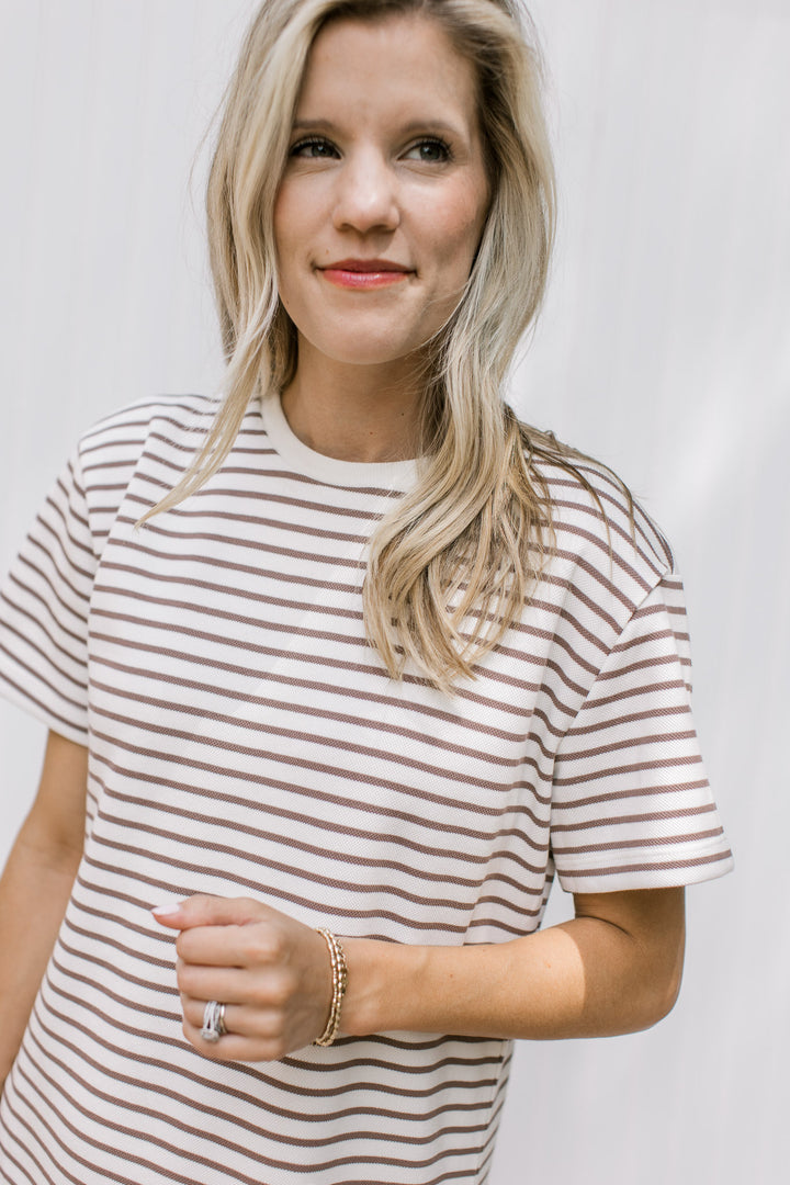 Close up of mocha stripes on a white casual dress with short sleeves and a round neck.