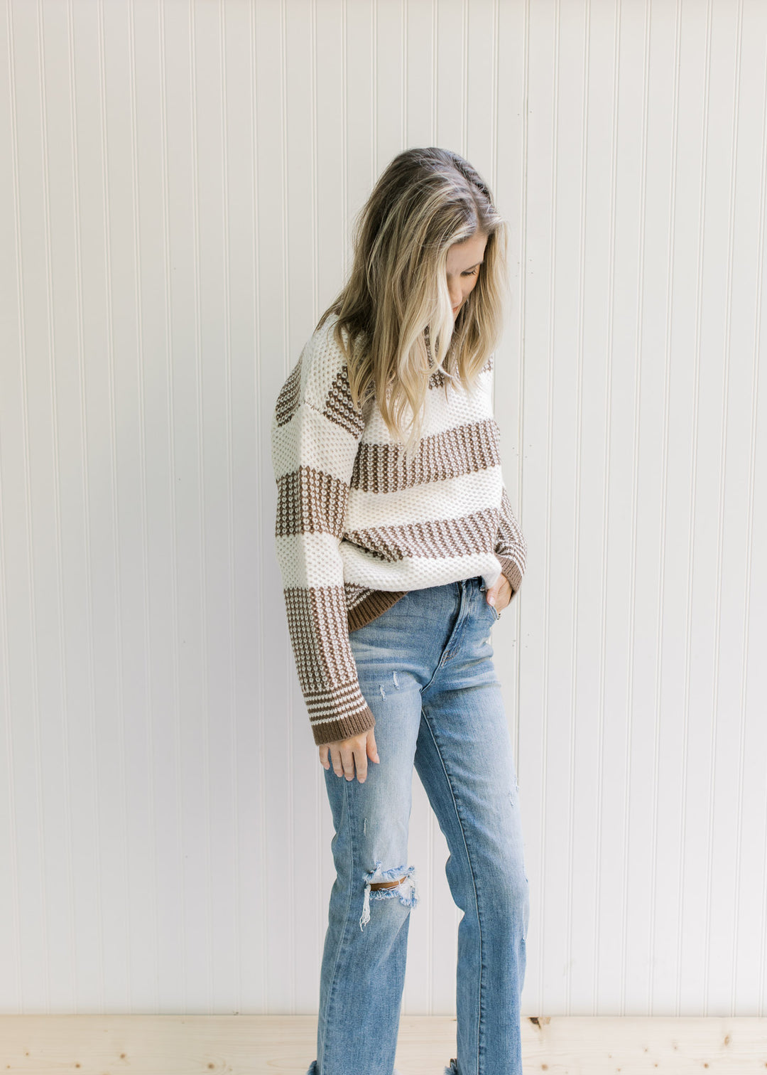 Model wearing jeans with a mocha and white striped sweater with a textured knit and long sleeves. 