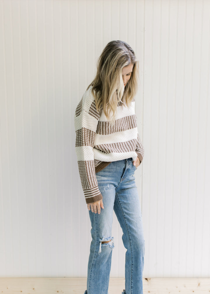 Model wearing jeans with a mocha and white striped sweater with a textured knit and long sleeves. 