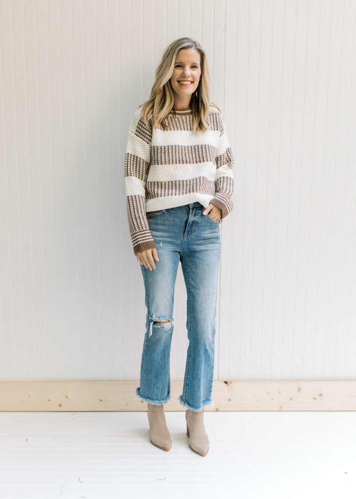 Model wearing jeans and booties with a mocha and white striped sweater with a textured knit. 