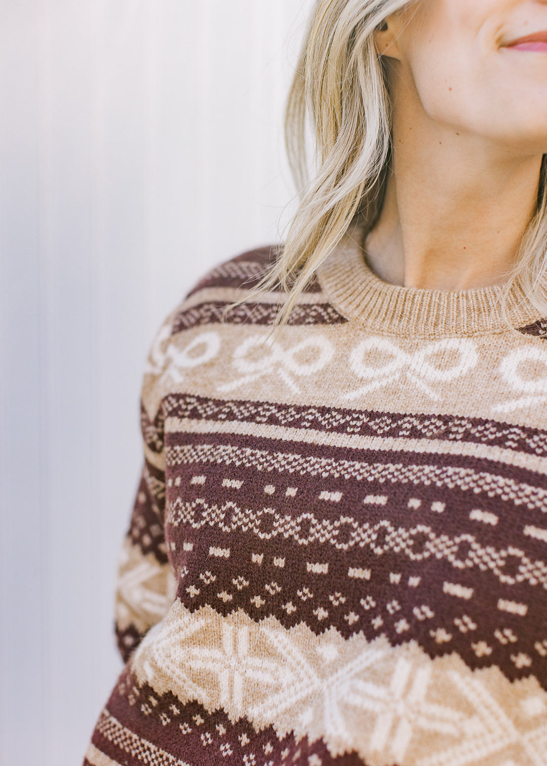 Close up of cream bows and taupe patterns in brown stripes of a long sleeve sweater. 