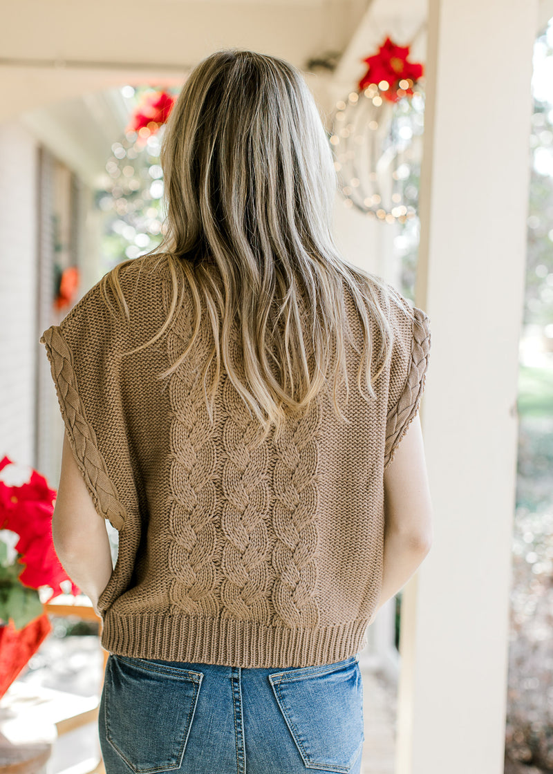 Back view of Model wearing a mocha cable knit sweater with capped sleeves and a round neck. 