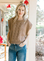 Model wearing jeans and a mocha cable knit sweater with capped sleeves and a round neck. 