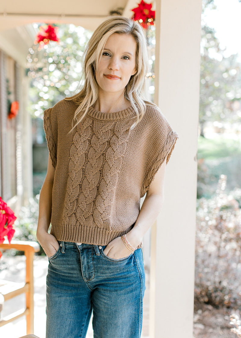 Model wearing jeans and a mocha cable knit sweater with capped sleeves and a round neck. 