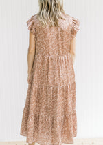 Back view of Model wearing a mocha, tiered midi with a blush floral pattern and flutter cap sleeves.